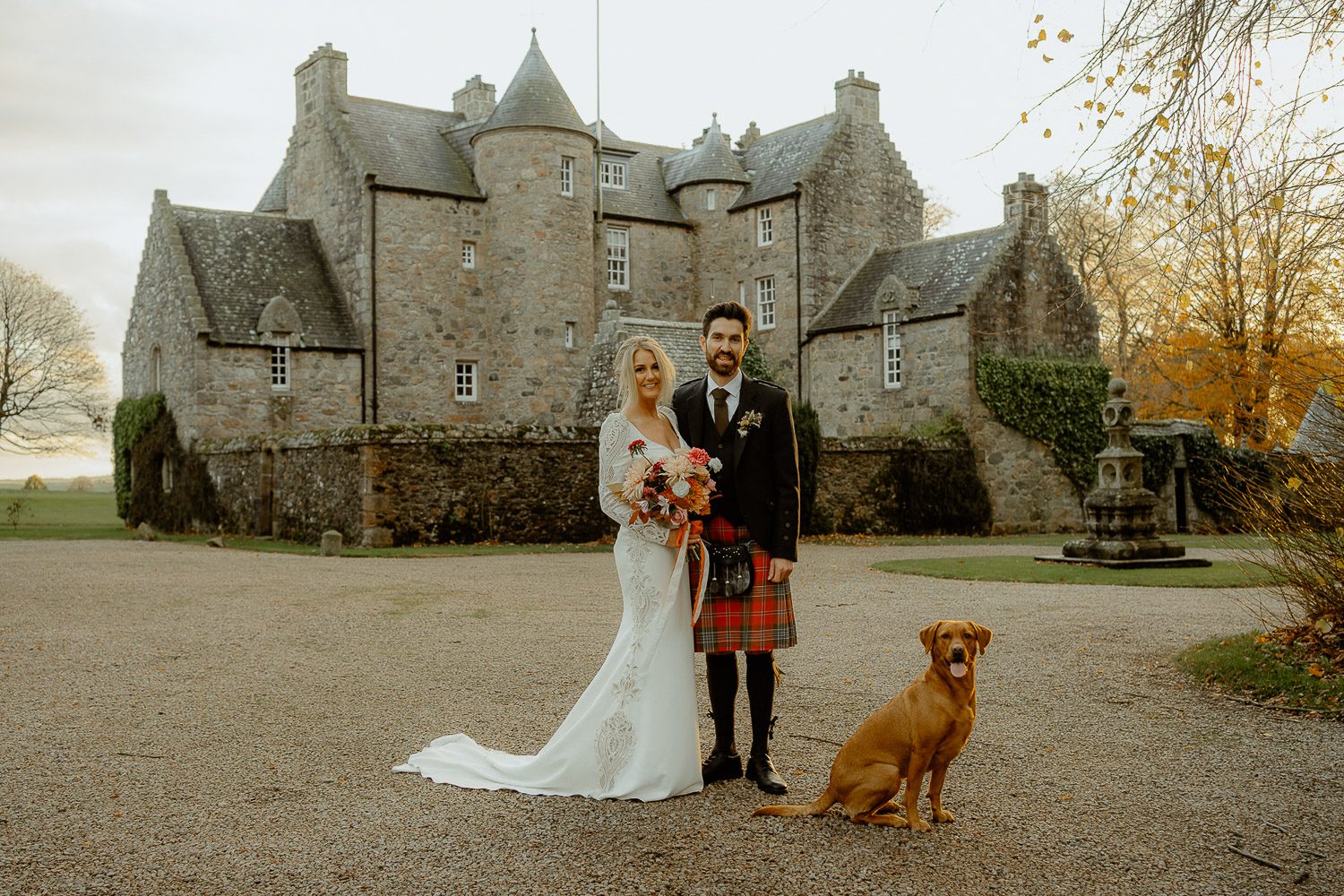 Bride and Groom holding each other next to dog in front of castle