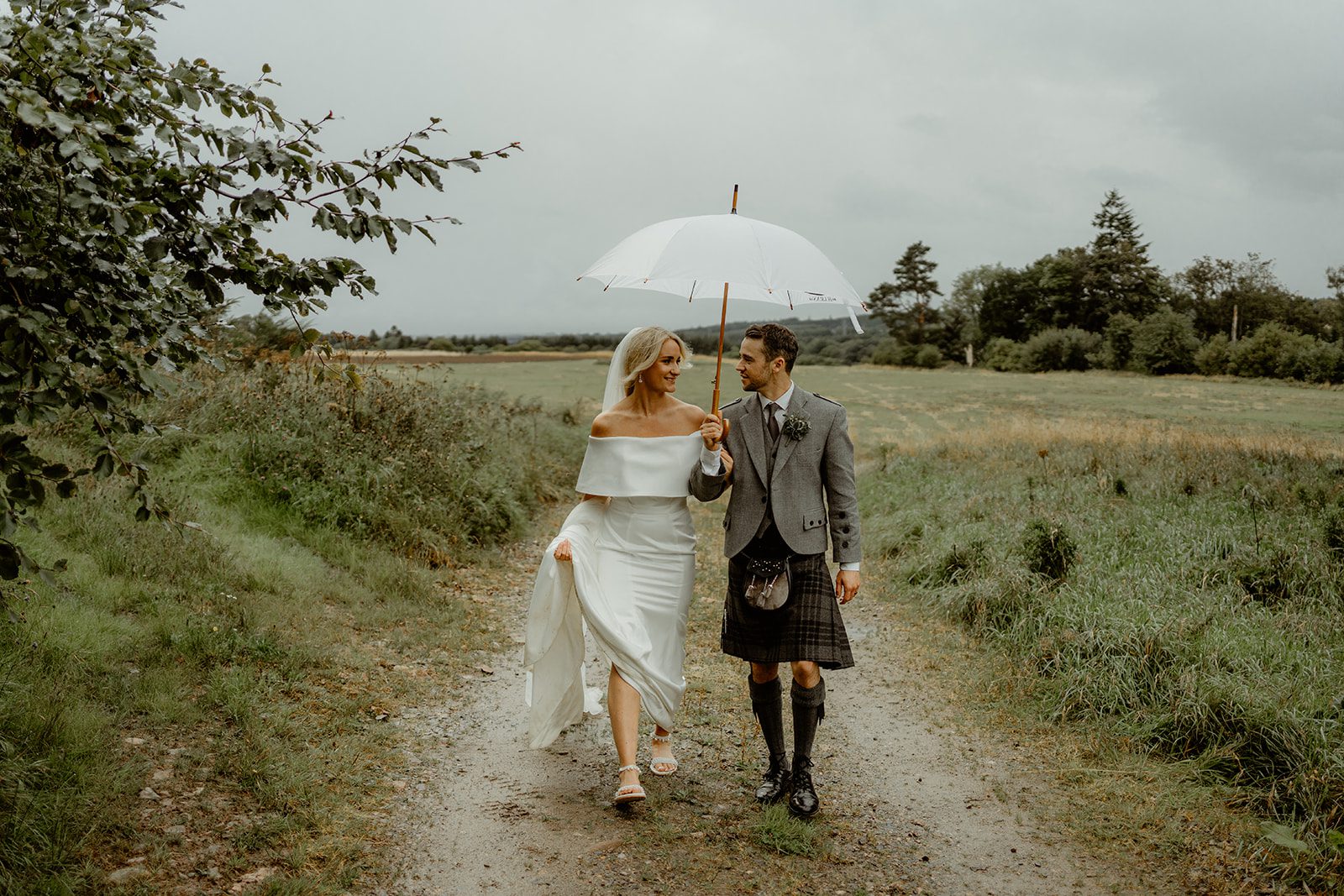 Bride and Groom walking holding an umbrella along farm lane